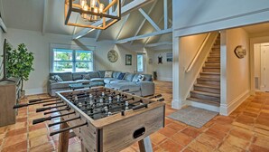 A spacious living area with a foosball table, a large window, a staircase, and a high ceiling with exposed beams.
