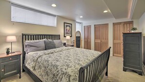 Quarto com cama, mesas de cabeceira, cômoda, espelho e janela com persianas.