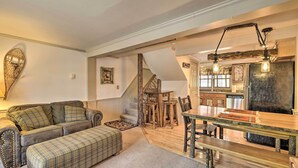 A cozy living room with a sofa, ottoman, and a dining area with a wooden table and chairs. - Townhome w/ Deck: Walk to Mirror Lake & Main St! (Lake Placid)