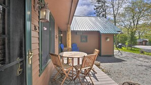 A wooden deck with a round table and four chairs, a small building with a green roof, and a blue chair outside. - Townhome w/ Deck: Walk to Mirror Lake & Main St! (Lake Placid)