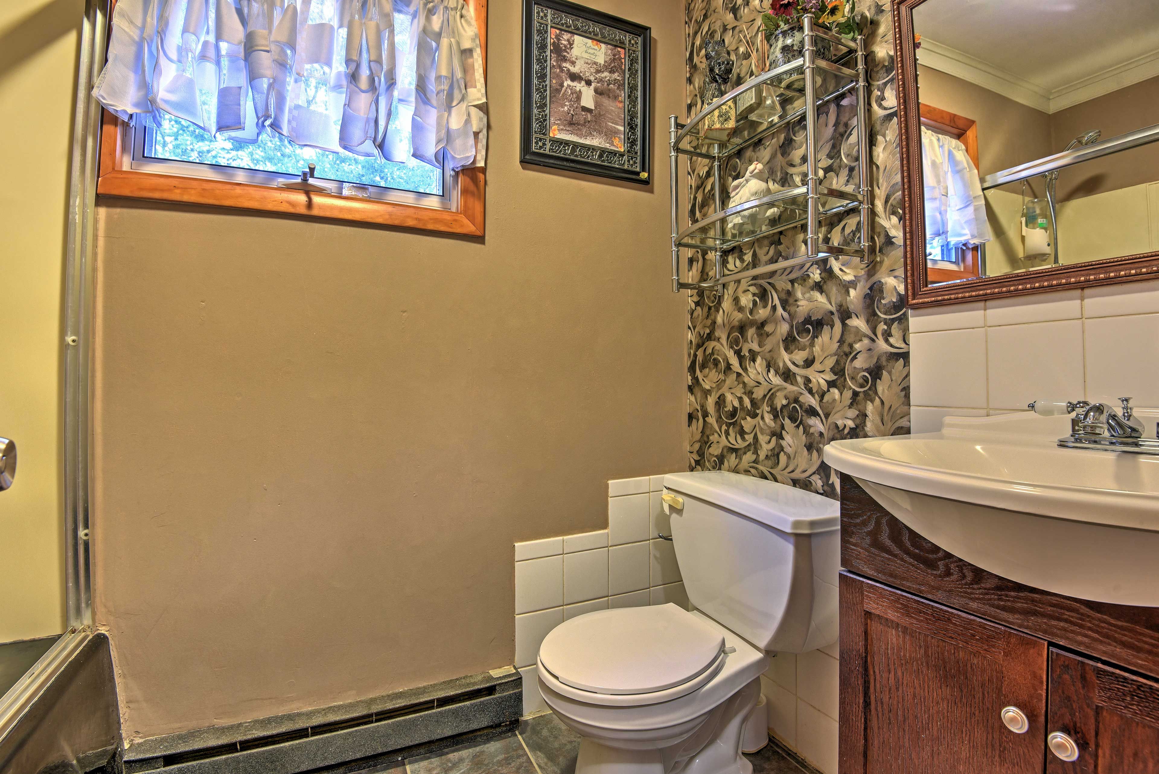 A bathroom with a toilet, a sink, a shower, and a window with curtains.