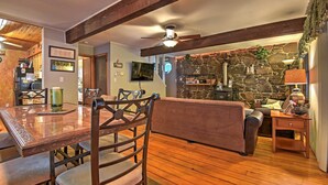 Uma sala de estar acolhedora com lareira de pedra, vigas de madeira, uma mesa de jantar com cadeiras e uma televisão.