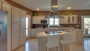 Une cuisine moderne avec des meubles blancs, un îlot central doté de tabourets, une hotte de cuisine en acier inoxydable et un four à micro-ondes.