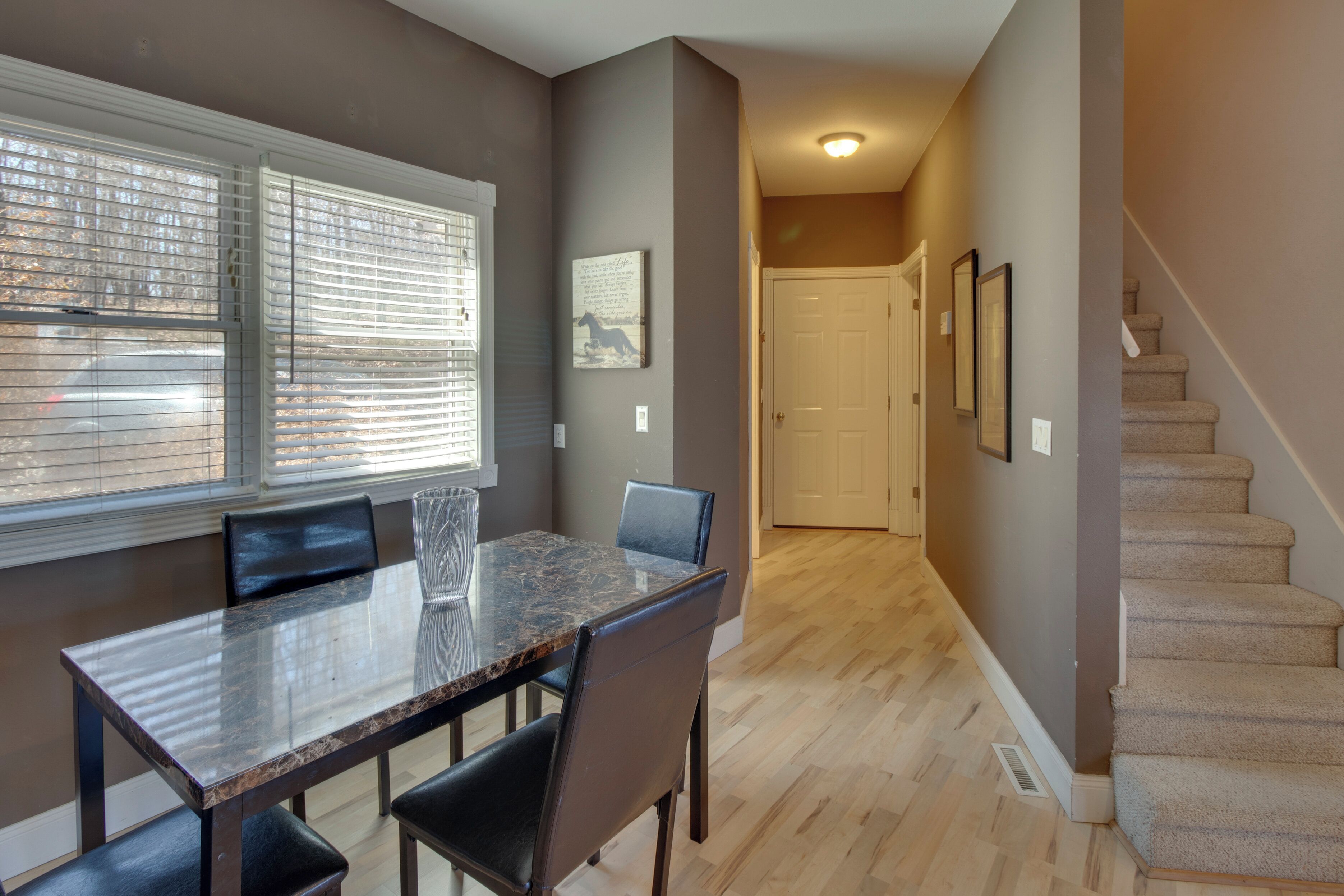 A dining area with a glass-top table and chairs, a window with blinds, and a staircase leading to another room.