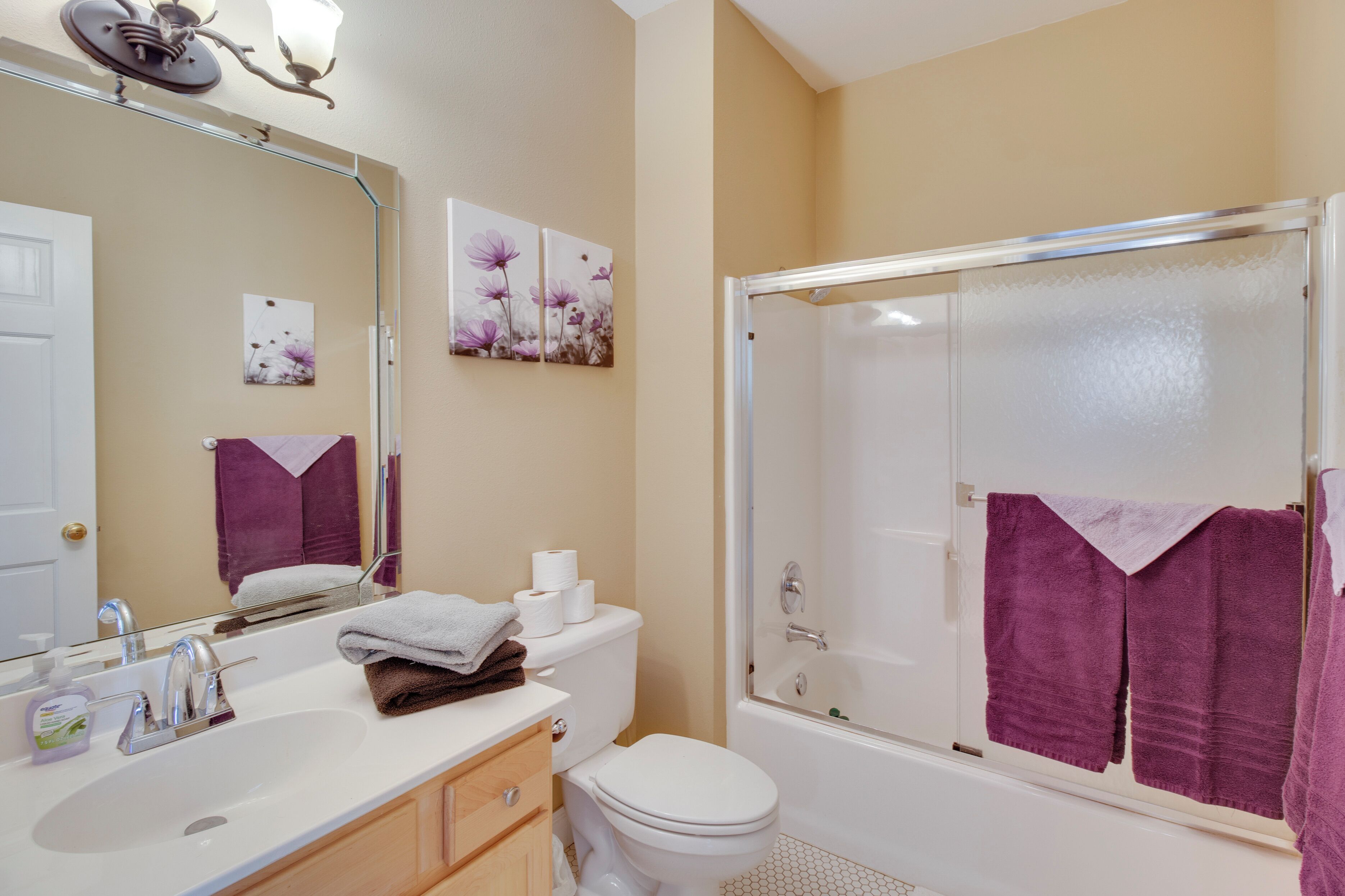 A bathroom with a white sink, toilet, and bathtub. There are purple towels hanging on the wall and a glass shower enclosure.