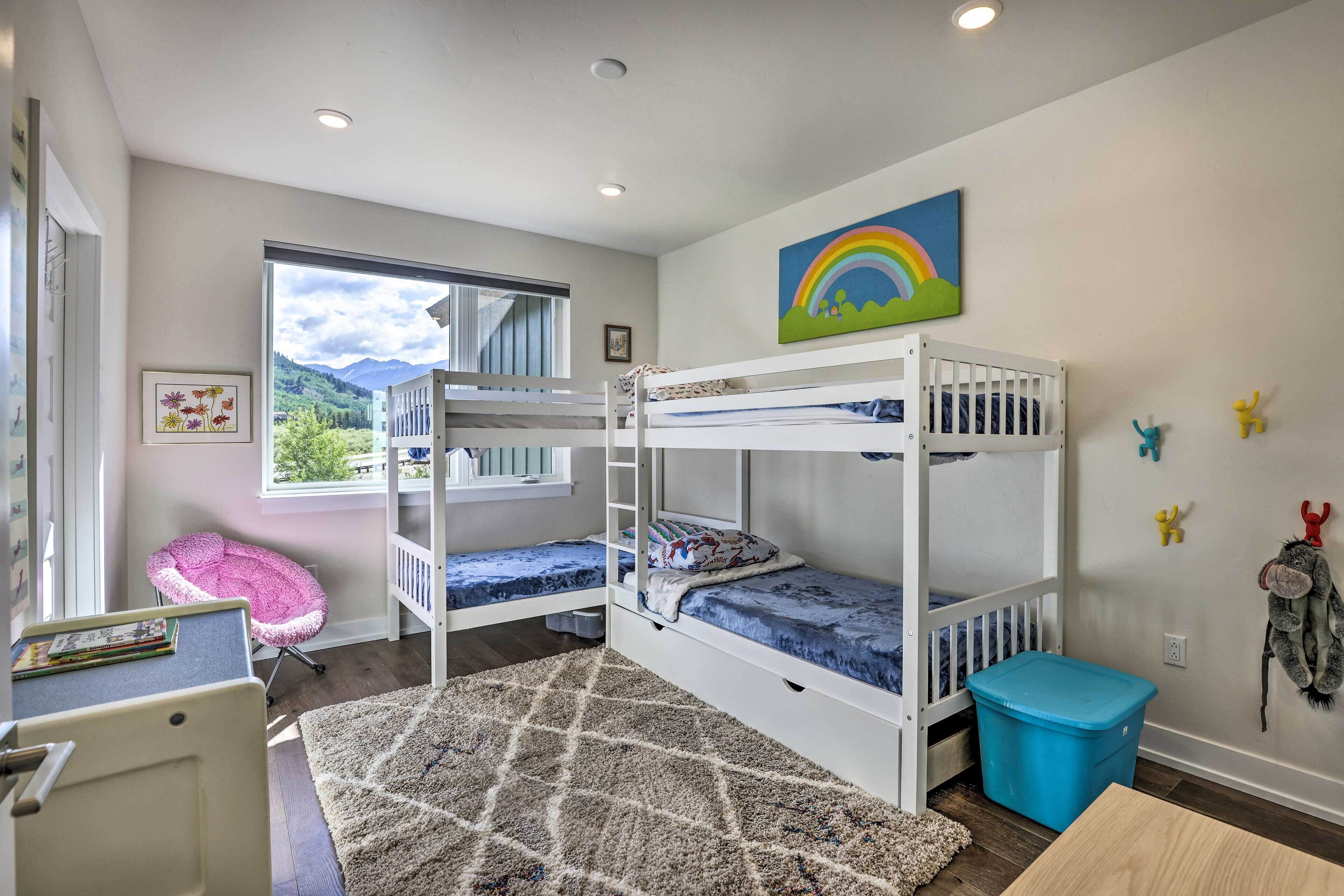 Une chambre d’enfant avec des lits superposés, un bureau, une chaise, un tapis et une fenêtre donnant sur un paysage montagneux.