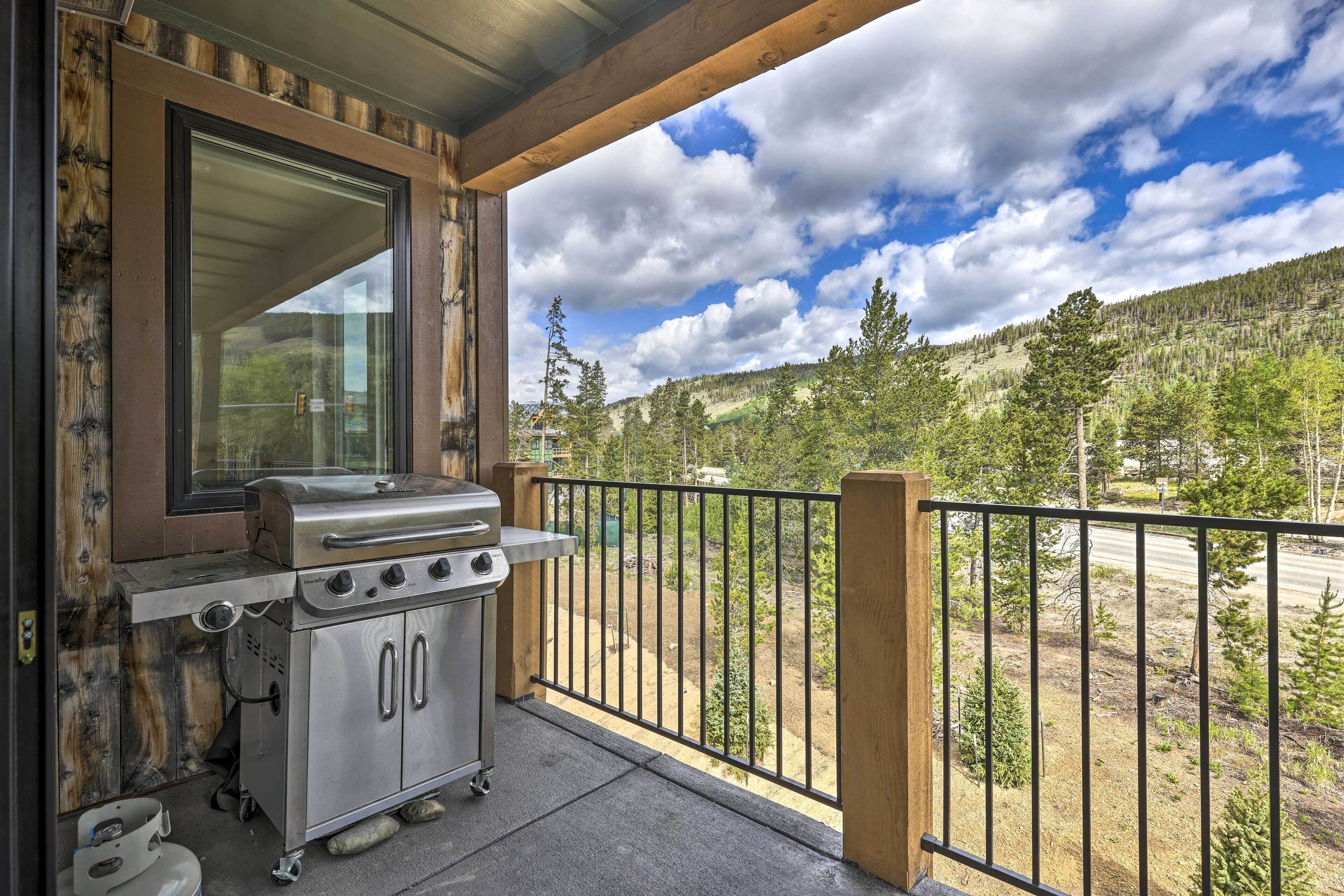 A balcony with a grill, a window, and a view of a forested hillside.