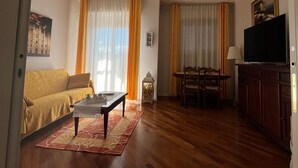 Un saló amb un sofà, una taula baixa, una televisió i una zona de menjador amb taula i cadires.