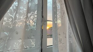 Una finestra amb cortines florals lleugeres, que deixa entreveure una vista del capvespre.