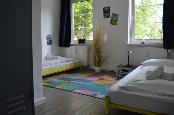 A bedroom with two beds, a colorful rug, and a window with curtains.