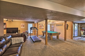 A living room with a pool table, a treadmill, and a leather couch. - Deluxe Omaha Escape w/ Game Room, Pool Access (Omaha)