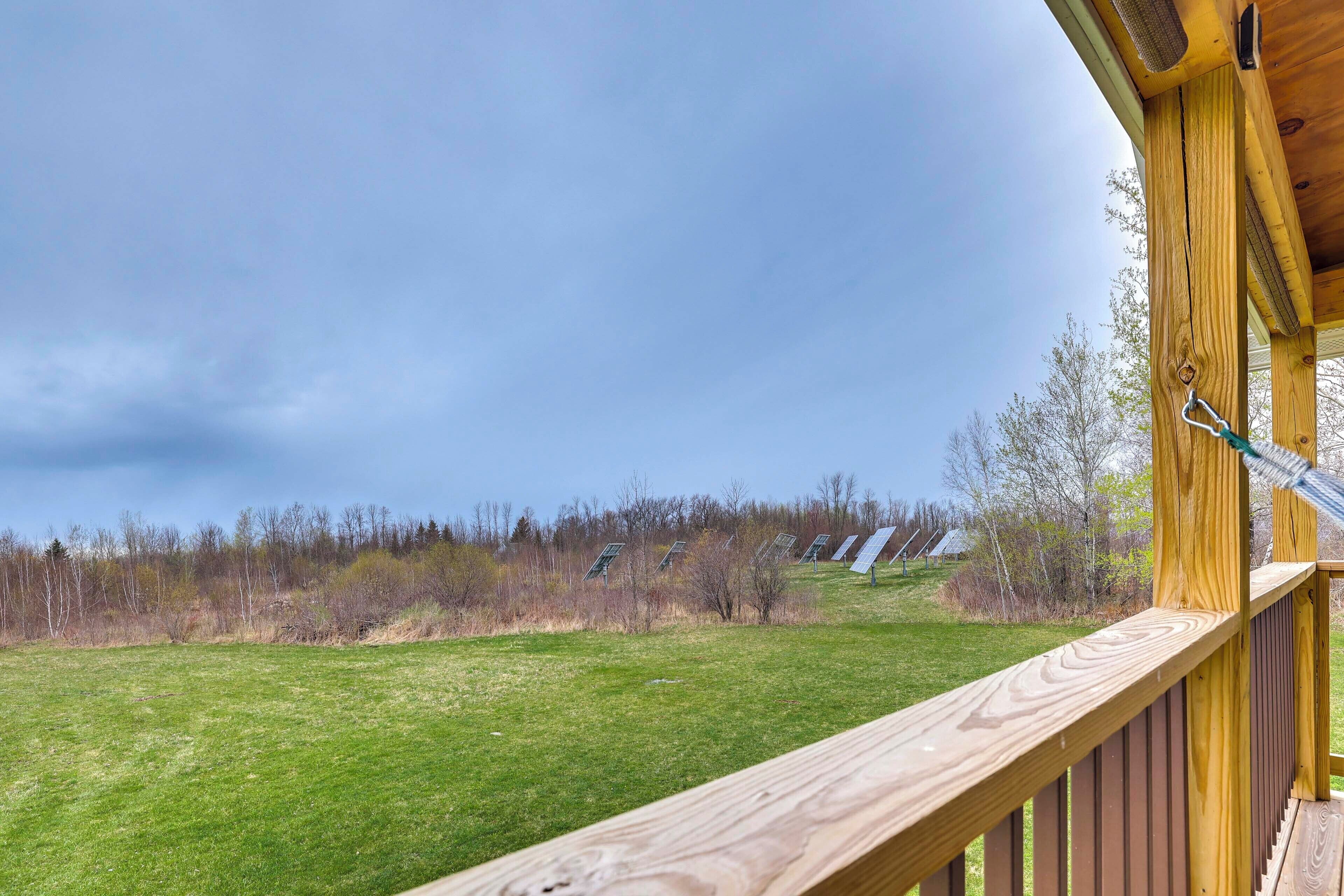 A wooden deck with a view of a grassy field and solar panels in the distance.