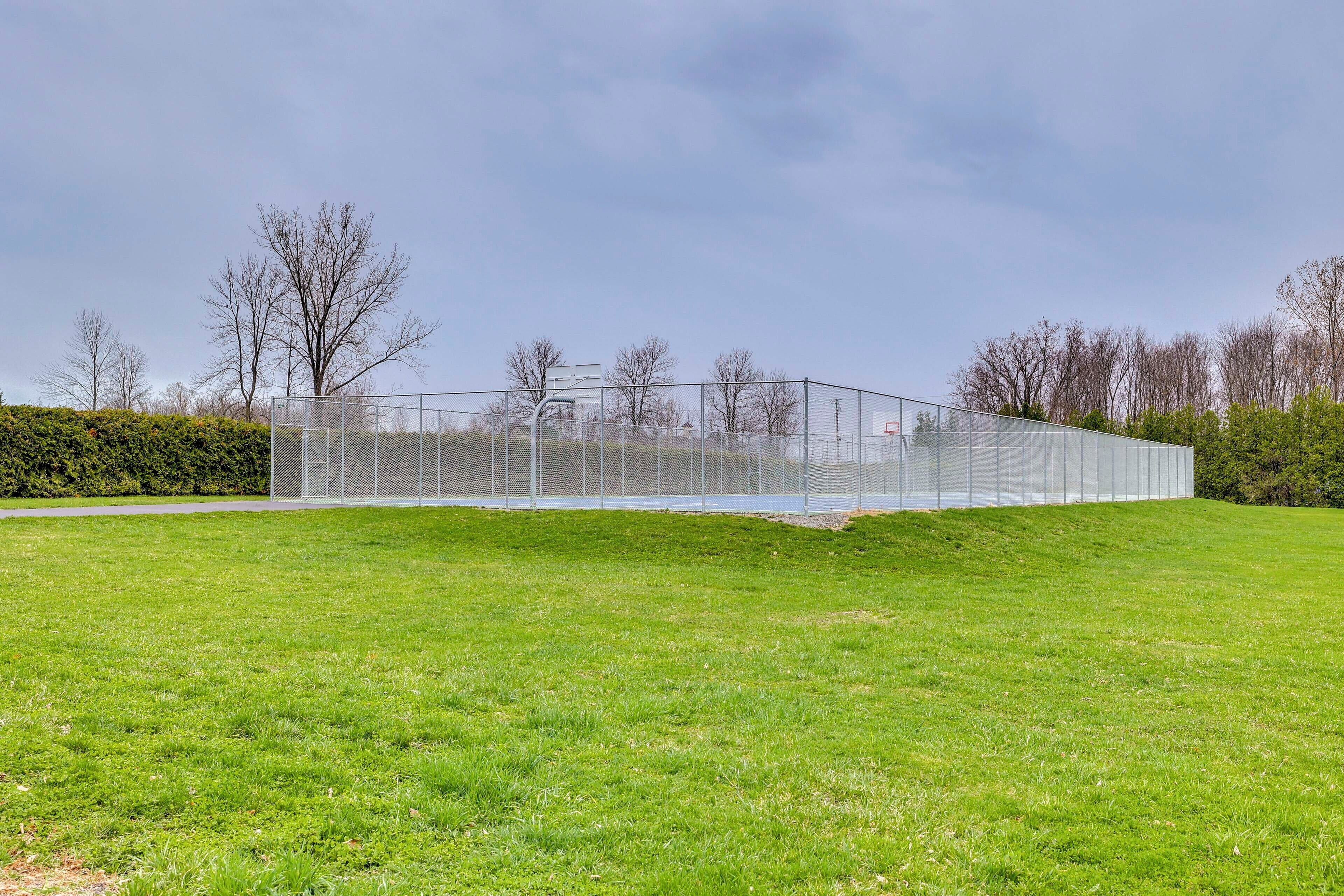 A modern sports facility with a basketball court, surrounded by a green field and trees.