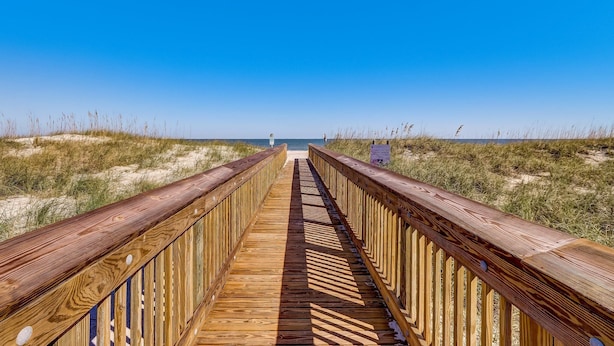 Un paseo marítimo de madera que conduce a una playa con cielos despejados.
