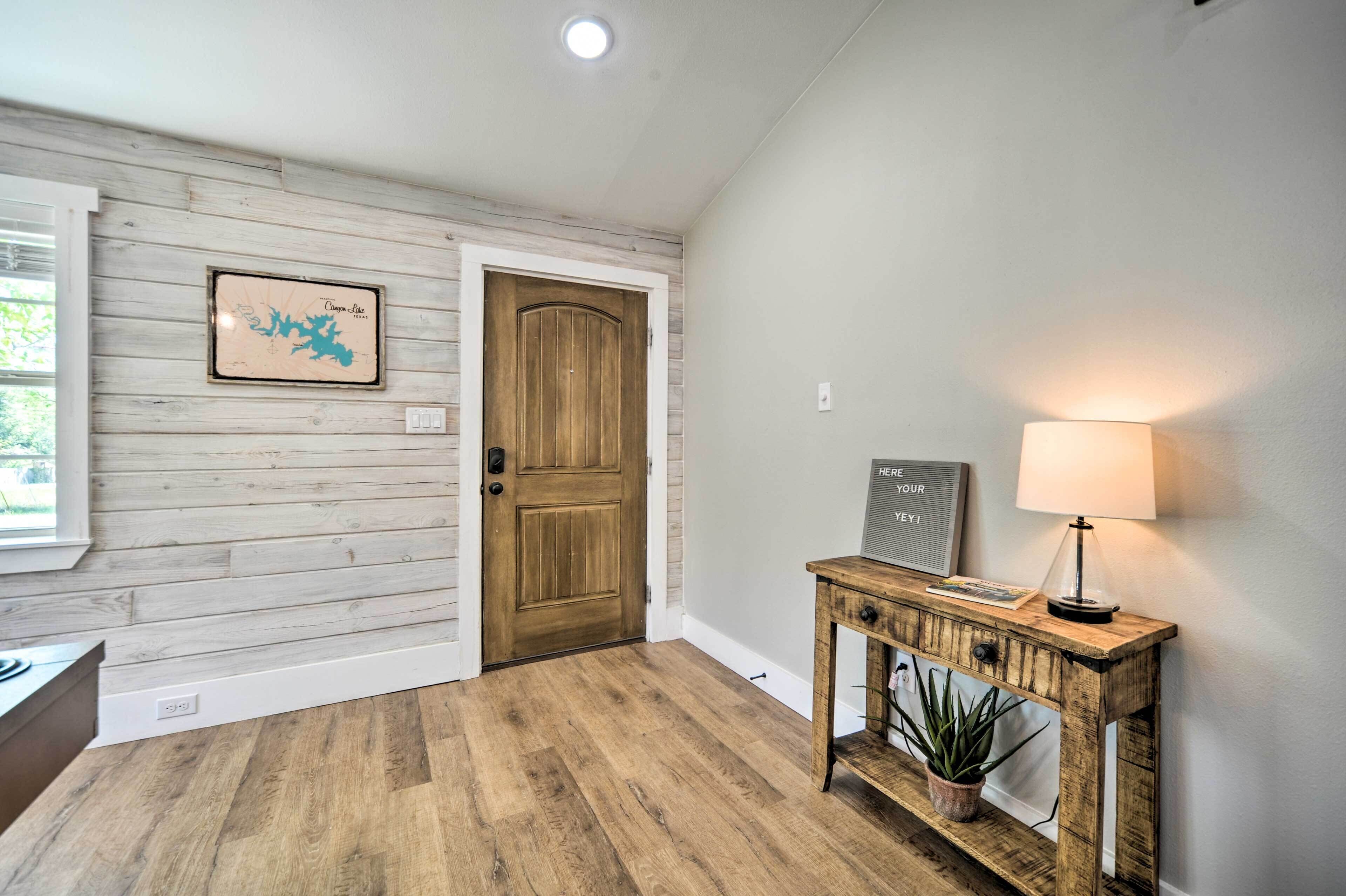 Un pasillo con una puerta de madera, un mapa enmarcado, una consola con una lámpara y una planta en maceta.