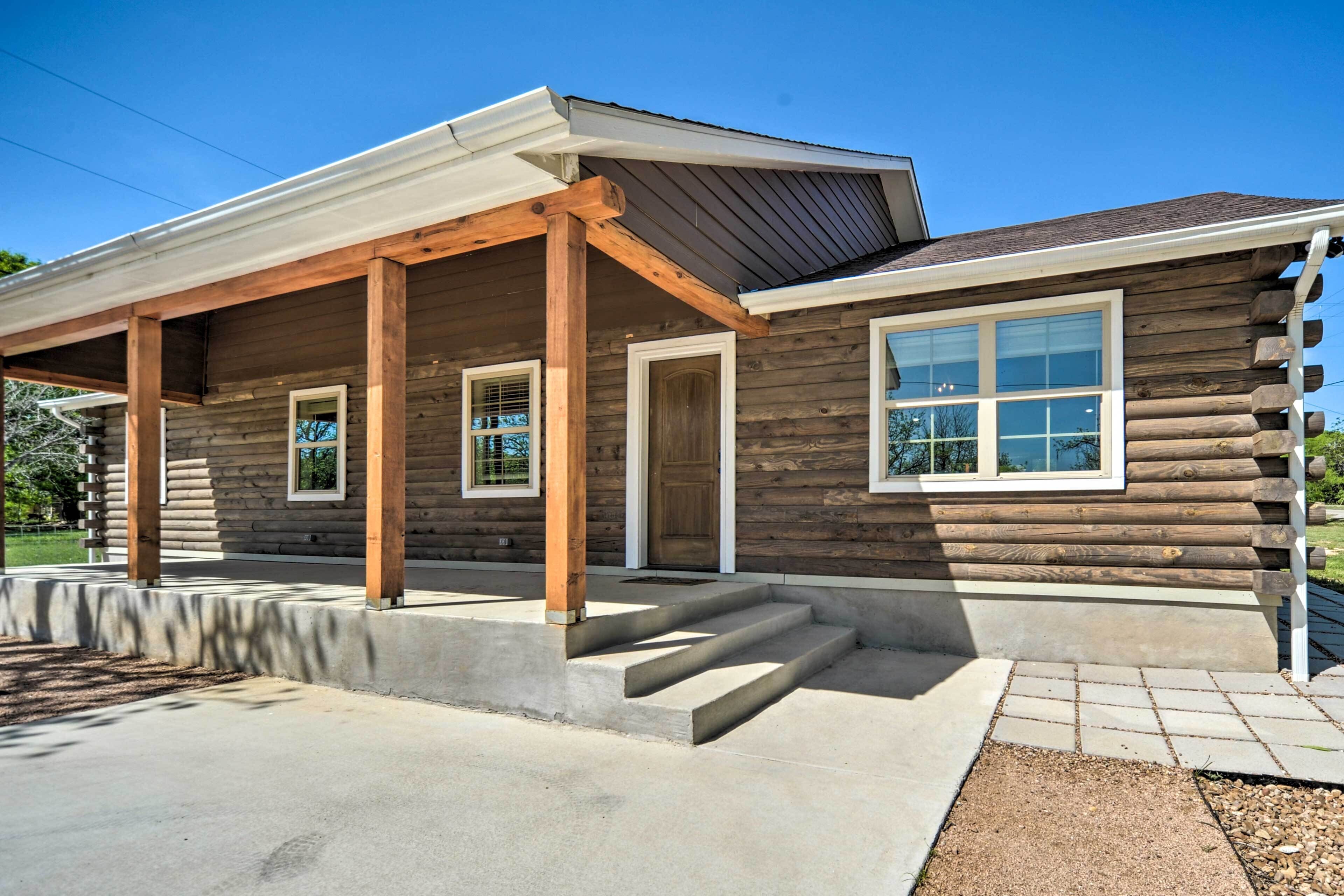 A log cabin with a covered porch, a front door, and a large window.