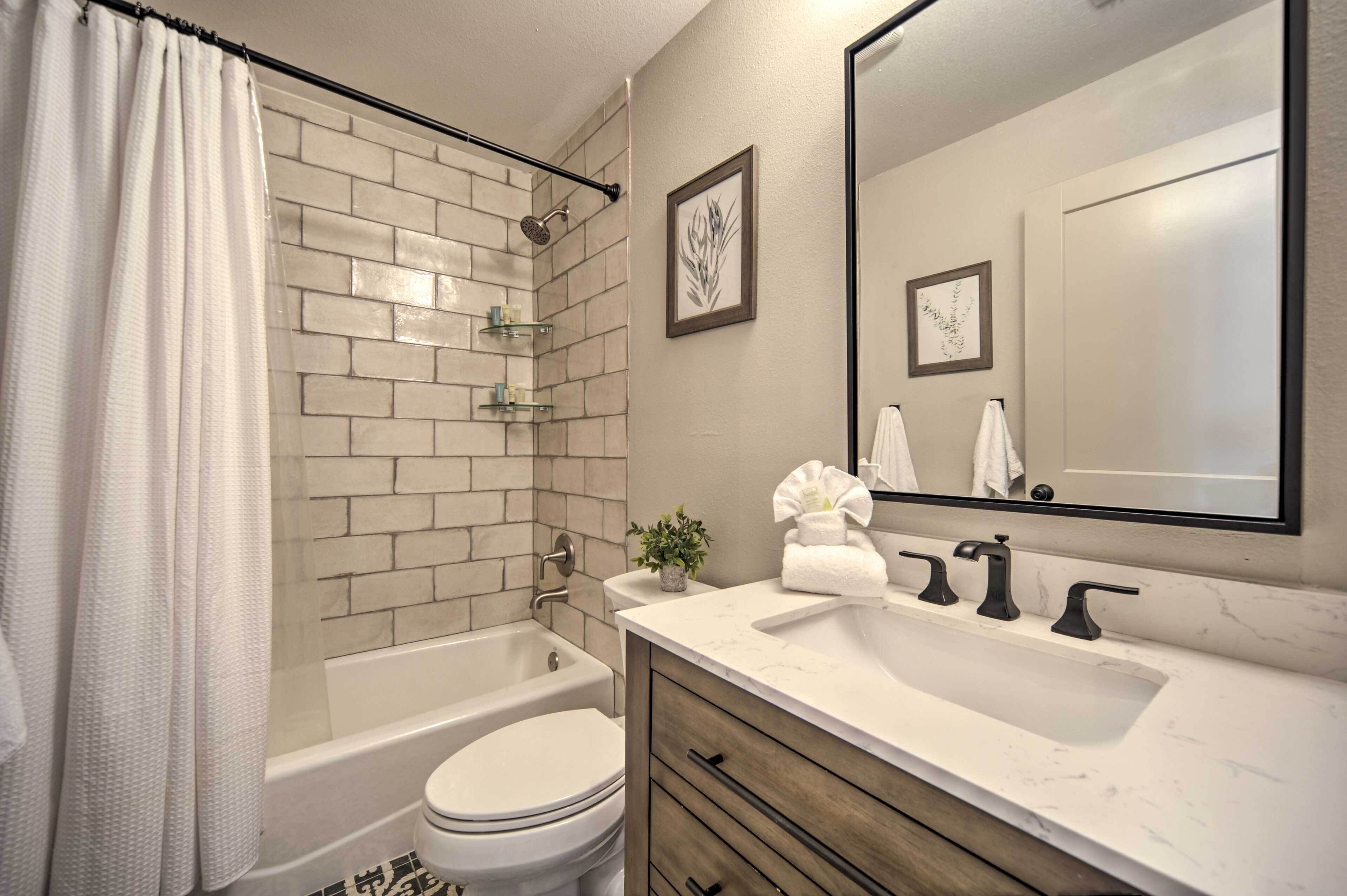 A modern bathroom with a white bathtub, a toilet, a sink with a marble countertop, and a shower with a glass enclosure.