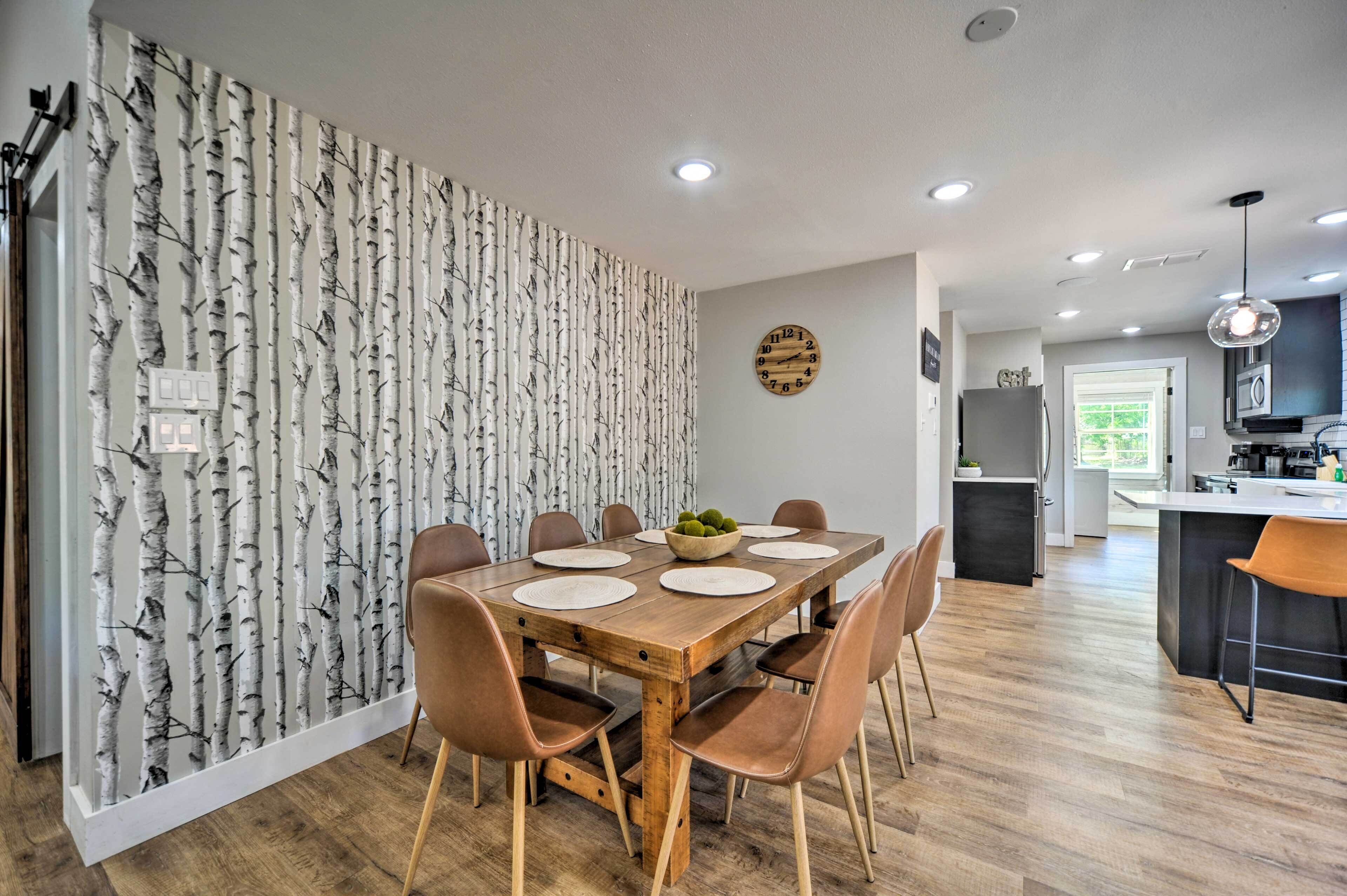 Un coin repas avec une table en bois, six chaises et un mur décoratif recouvert d’un papier peint représentant des bouleaux.