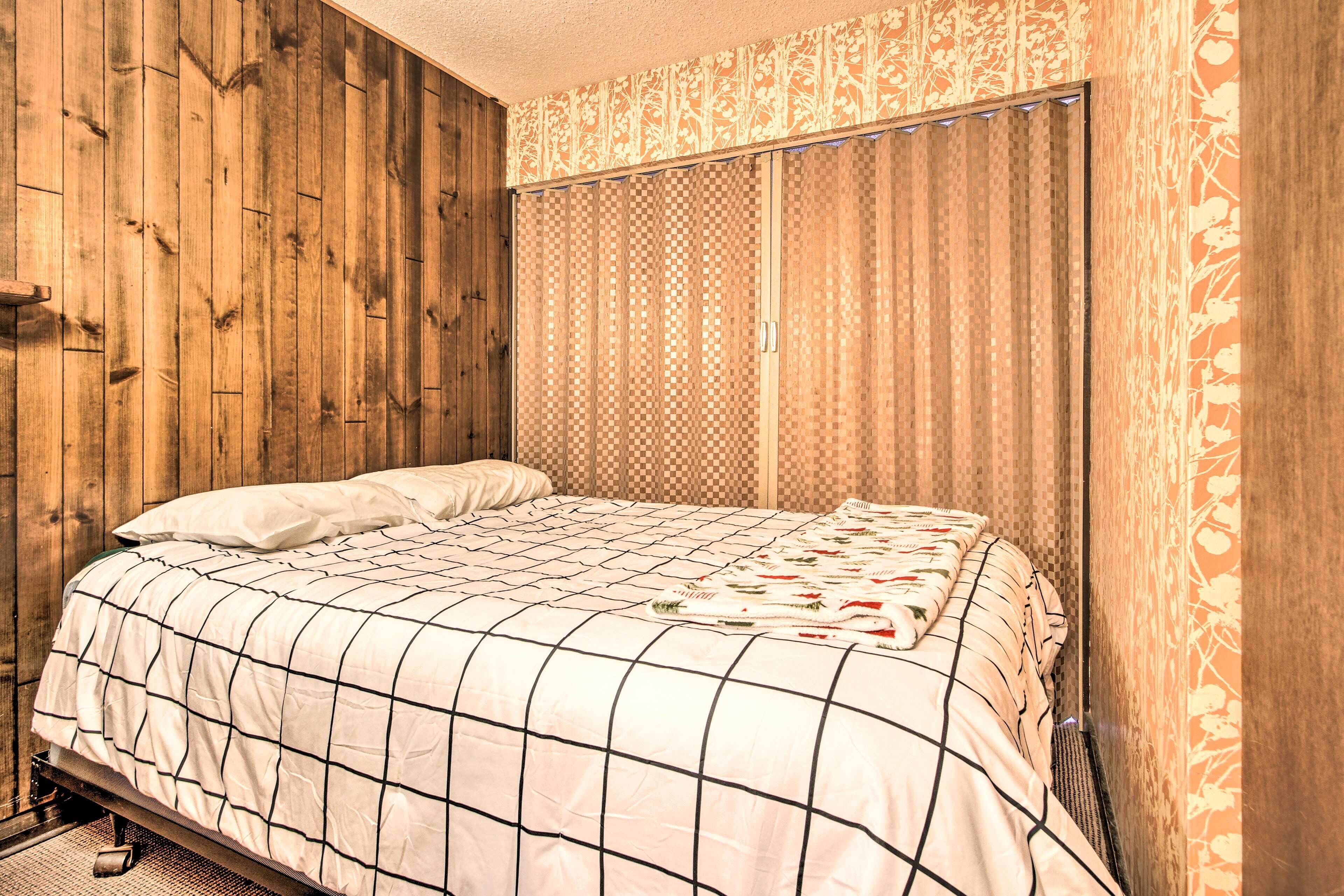 A bedroom with a wooden wall, a checkered bedspread, and a patterned curtain.
