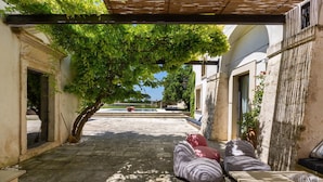 Un espace extérieur aménagé avec un coin salon, une pergola, un sol en pierre et une vue sur une piscine en arrière-plan.