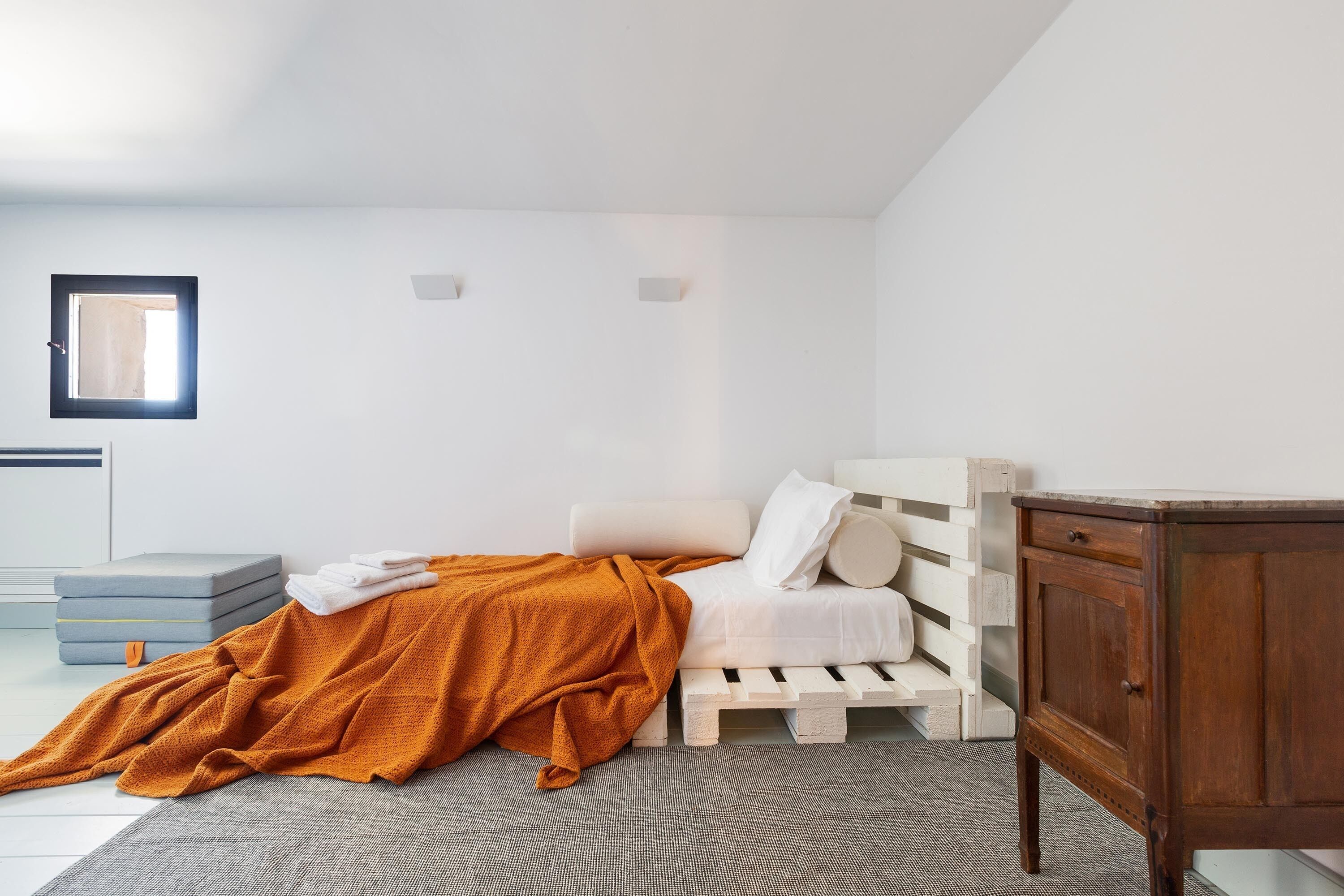 A bedroom with a bed, a wooden nightstand, a window, and a small table.