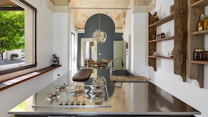 Une cuisine moderne dotée d’un îlot central, d’une arche en pierre, d’étagères en bois et offrant une vue sur l’extérieur.