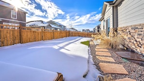 A snow-covered backyard with a wooden fence, a stone wall, and a paved walkway. - 10 Mi to Dia: Spacious Aurora House w/ Yard! (Aurora)