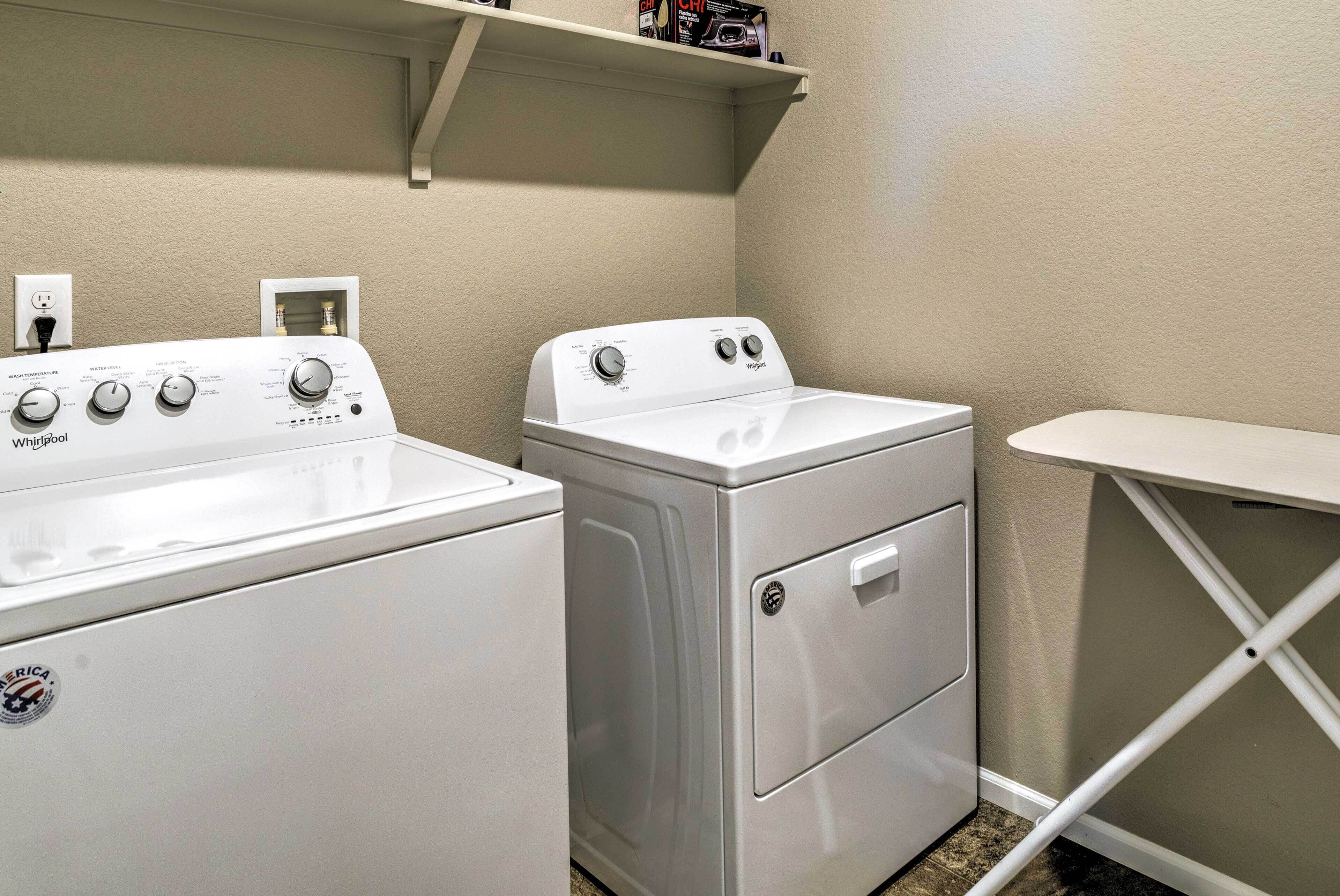 A laundry room with two Whirlpool washers and a dryer, a shelf above the dryers, and a white folding table.