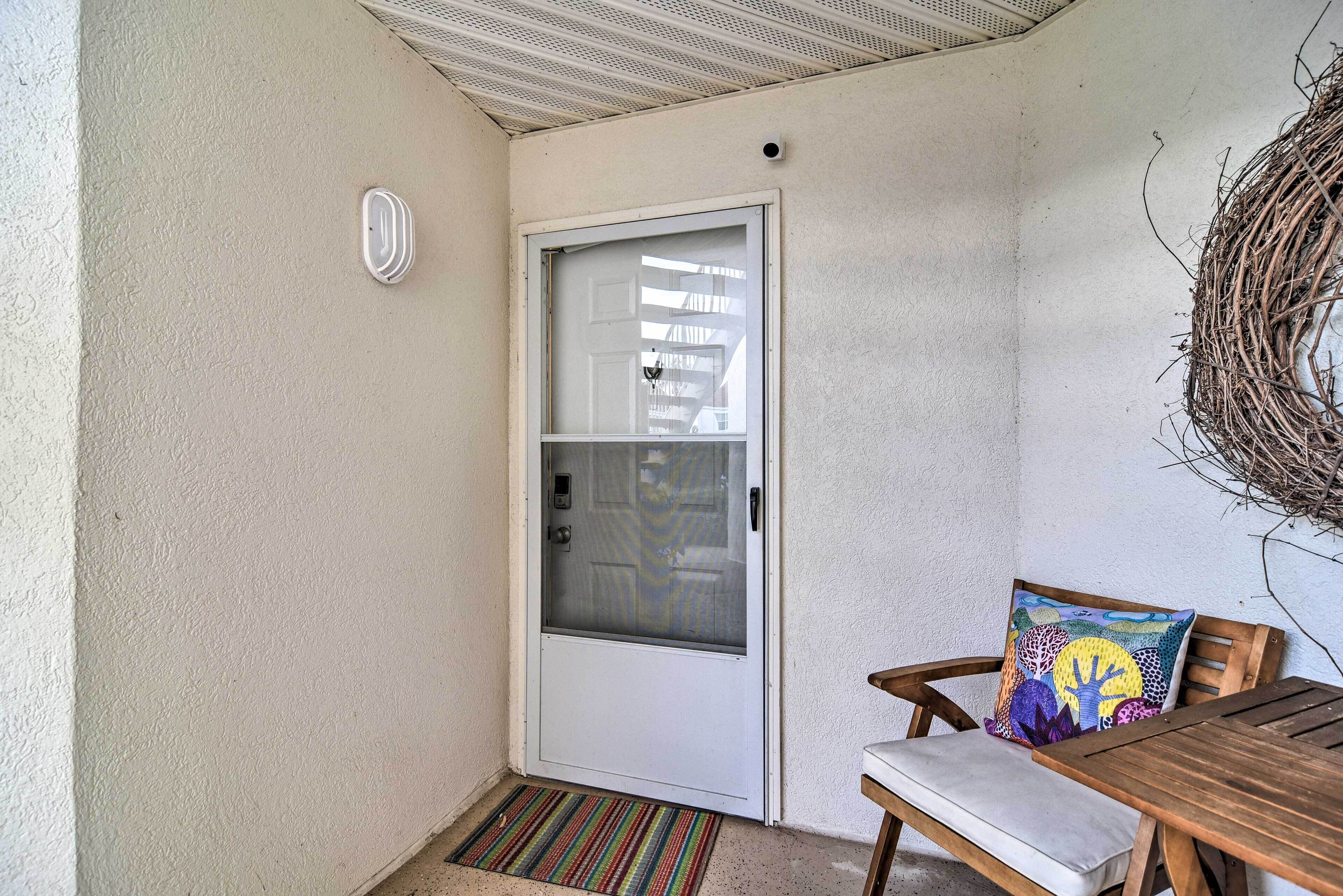 A door with a frosted glass panel, a white doormat, a wooden bench with a cushion, and a woven wall decoration.