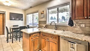 A kitchen with granite countertops, wooden cabinets, a dishwasher, and a dining area with a table and chairs. - Vancouver Home w/ Hot Tub < 15 Mi to Portland! (Vancouver)