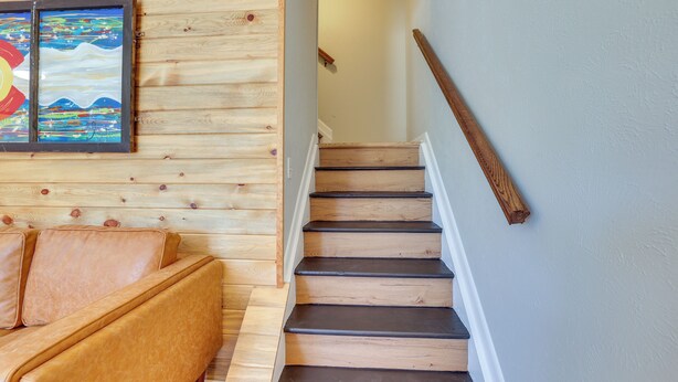 A wooden staircase with a handrail, a wooden wall paneling, and a sofa with cushions. - Quaint Winter Park Townhouse < 5 Mi to Ski! (Winter Park)