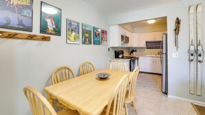 A dining area with a wooden table and chairs, a kitchen in the background, and skis mounted on the wall. - Quaint Winter Park Townhouse < 5 Mi to Ski! (Winter Park)