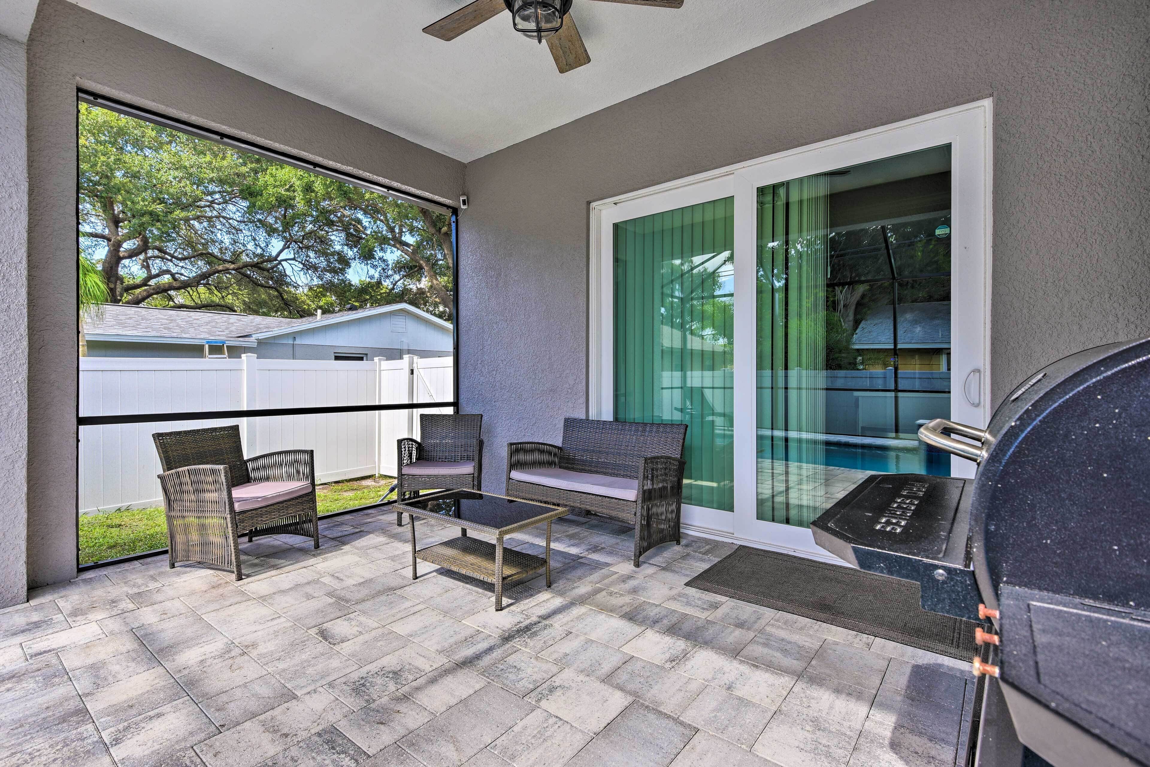 A covered patio with wicker furniture, a grill, and a view of a house and trees.