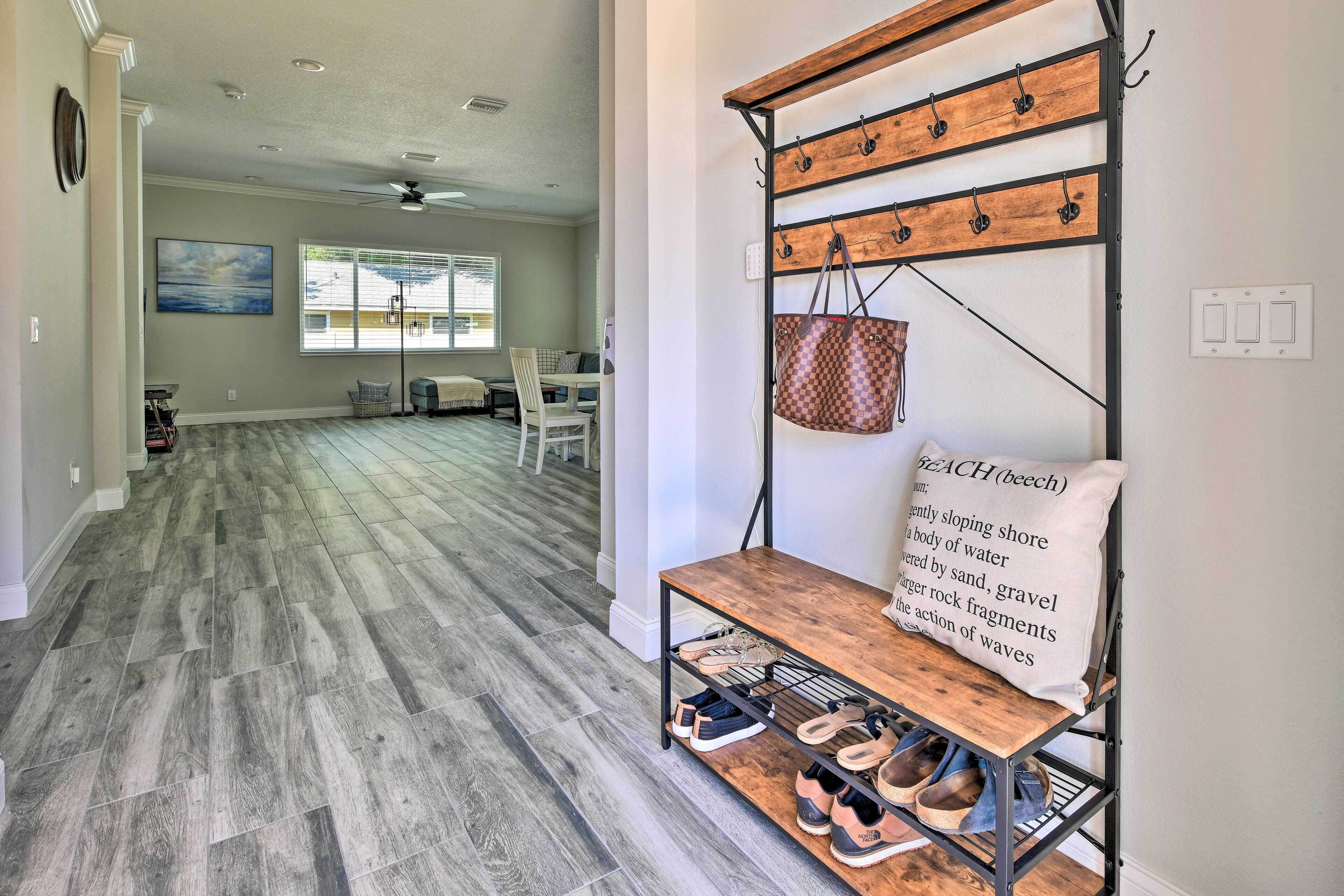 A spacious living area with a wooden floor, a dining table with chairs, and a wall-mounted shoe rack with a hanging bag.