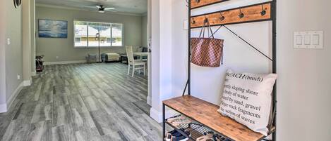 A spacious living area with a wooden floor, a dining table with chairs, and a wall-mounted shoe rack with a hanging bag.