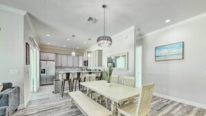 A modern kitchen with white cabinets, a central island, and a dining area with a wooden table and benches. - Beautiful Getaway ~ 4 Miles to Venice Beach! (Venice)