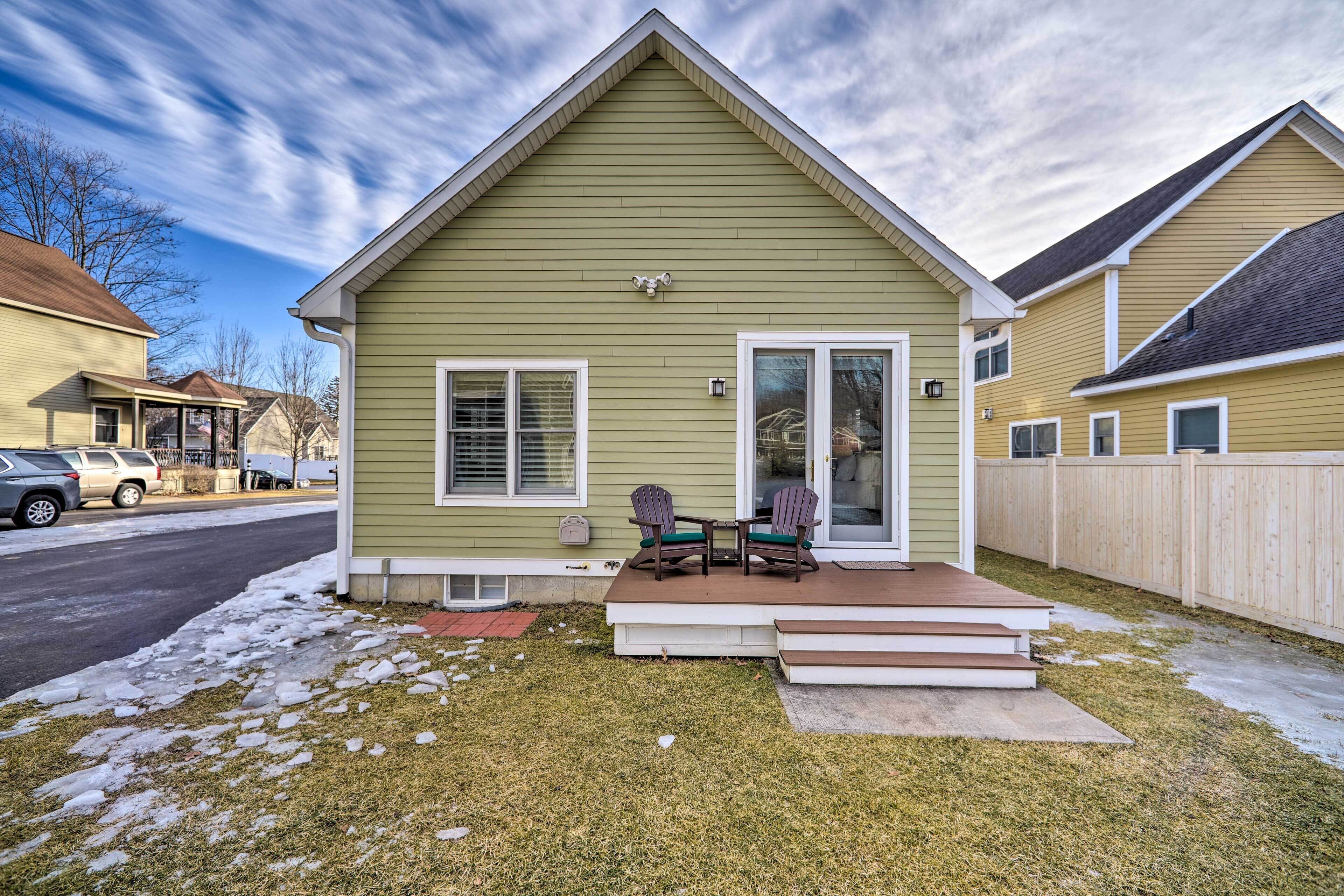 A single-story house with a green exterior, a front porch with two Adirondack chairs, and a small deck.