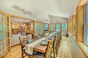 A long dining table set for a meal in a spacious room with wooden floors and large windows.