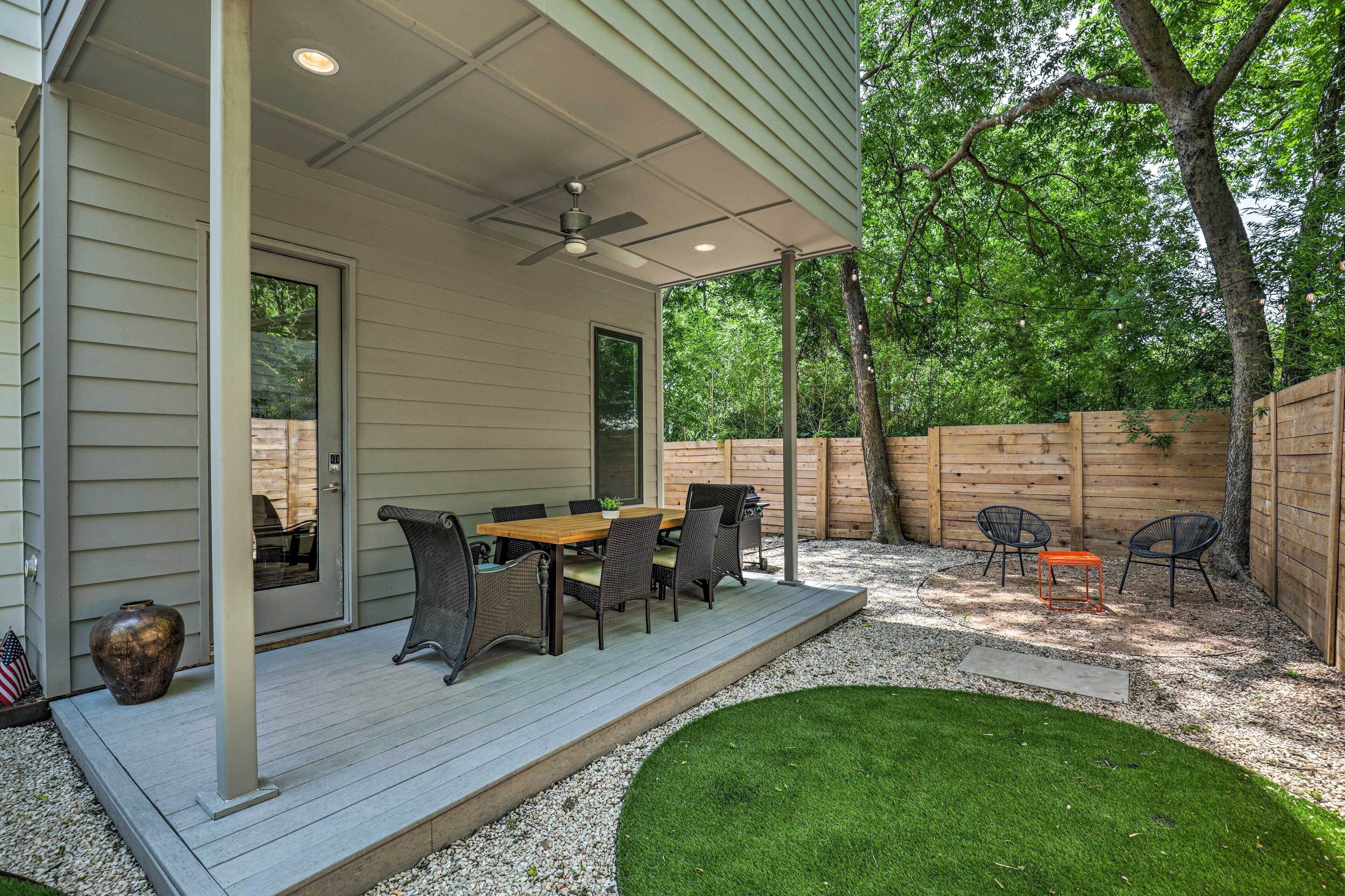 A covered patio with a dining table and chairs, a ceiling fan, and a wooden fence.