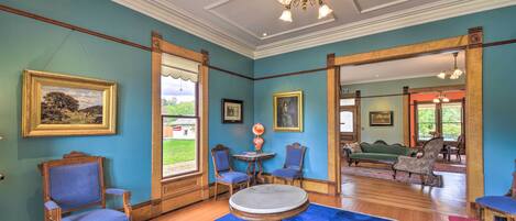 Una habitación con alfombra azul, sillas de madera, una mesa redonda y un candelabro.