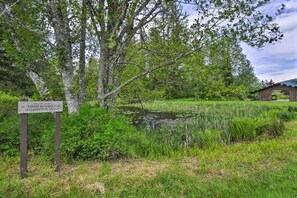 A wooden sign with a welcome message, a pond, and a rustic building in a natural setting.