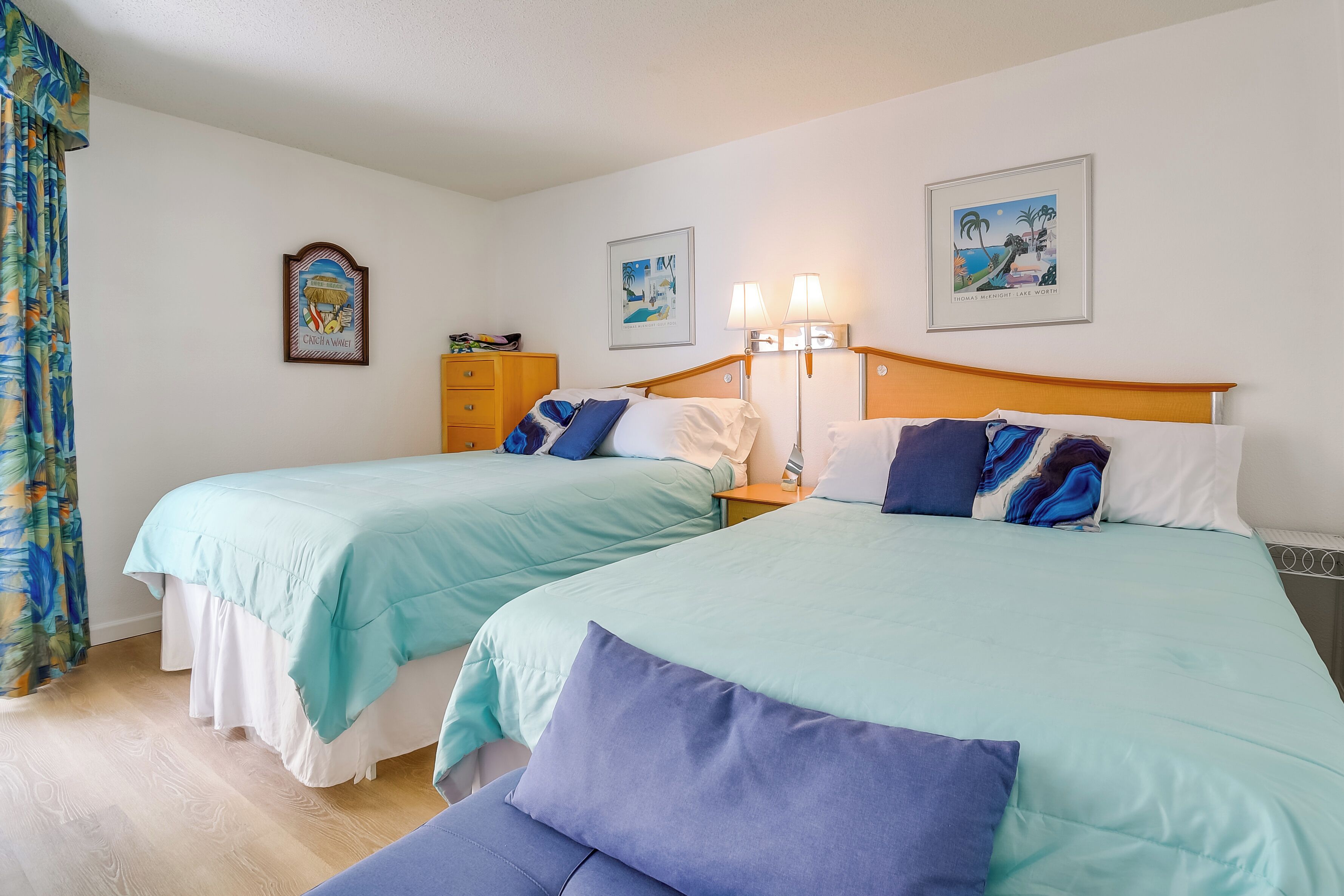 A hotel room with two beds, a wooden headboard, a nightstand, a lamp, and a framed picture on the wall.