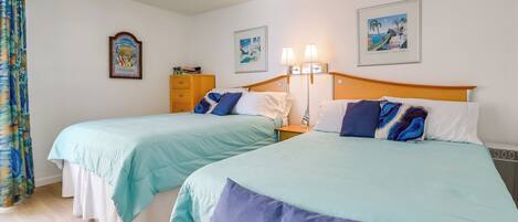 A hotel room with two beds, a wooden headboard, a nightstand, a lamp, and a framed picture on the wall.