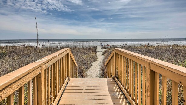 A wooden boardwalk leading to a beach with a fence in the background.