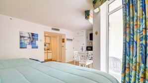 A bedroom with a bed, a dining area, and a kitchen visible through an open door.