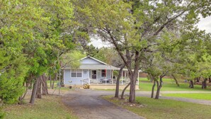 A small, single-story building with a porch and a covered entryway, surrounded by trees and a grassy area. - Canyon Lake Home w/ Resort Amenities & Fire Pit! (Canyon Lake)
