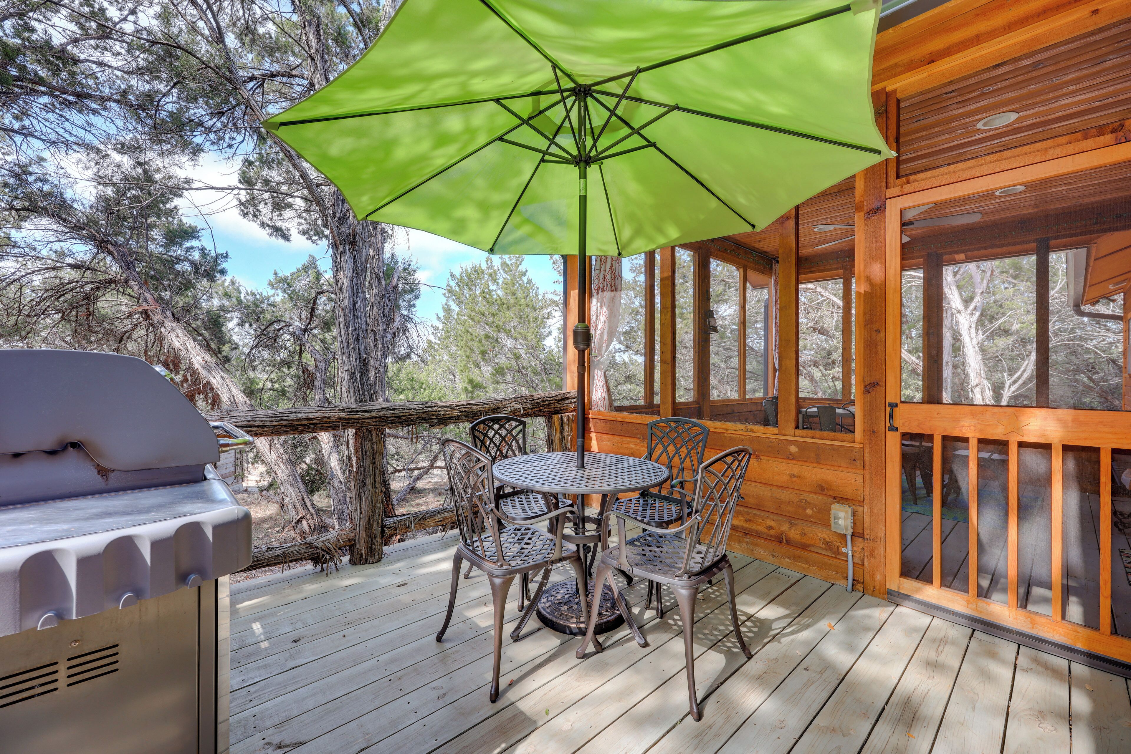 A wooden deck with a grill and a table with chairs under a green umbrella.