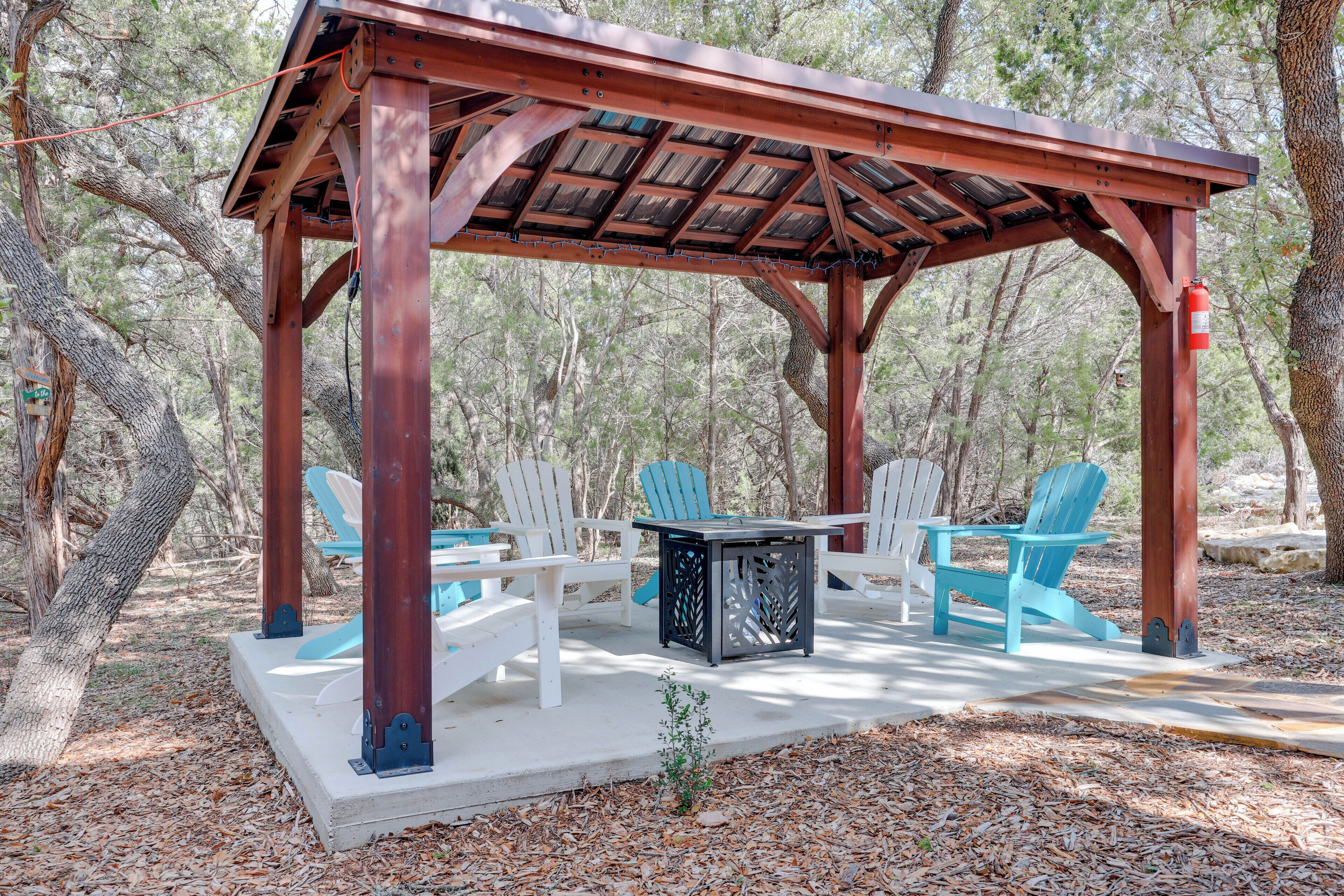 A wooden gazebo with a table and chairs in a wooded area.