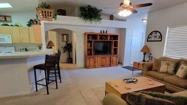 A living room with a sofa, a coffee table, and a TV stand. There is a kitchen area with cabinets and a microwave. - NEW! FAMILY FUN, ALOHA, Tropical Jericho with POOL (Lake Havasu City)