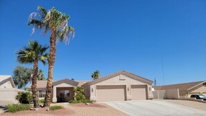 A single-story house with a garage, a driveway, and palm trees. - NEW! FAMILY FUN, ALOHA, Tropical Jericho with POOL (Lake Havasu City)